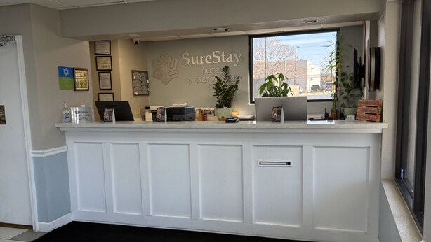 A hotel reception area with a reception desk, framed certificates, a large window, and a potted plant. - Cozy 1 - room hotel in charming Columbus and Ft. Moore with AC, WiFi (Columbus)