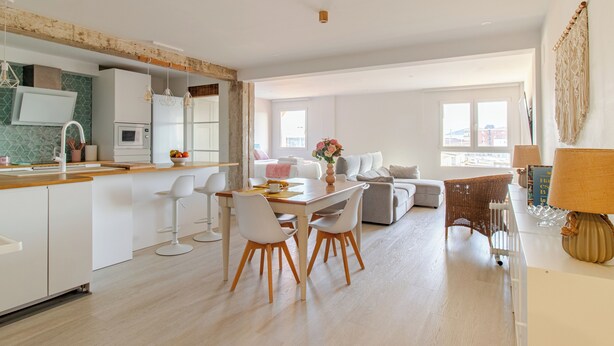 Een moderne keuken met witte kasten, een houten aanrechtblad en een eethoek met witte stoelen en een tafel.