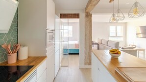 Een moderne keuken met houten aanrechtbladen, een inbouwoven en een eethoek met een houten tafel en hangende pendantlampen.