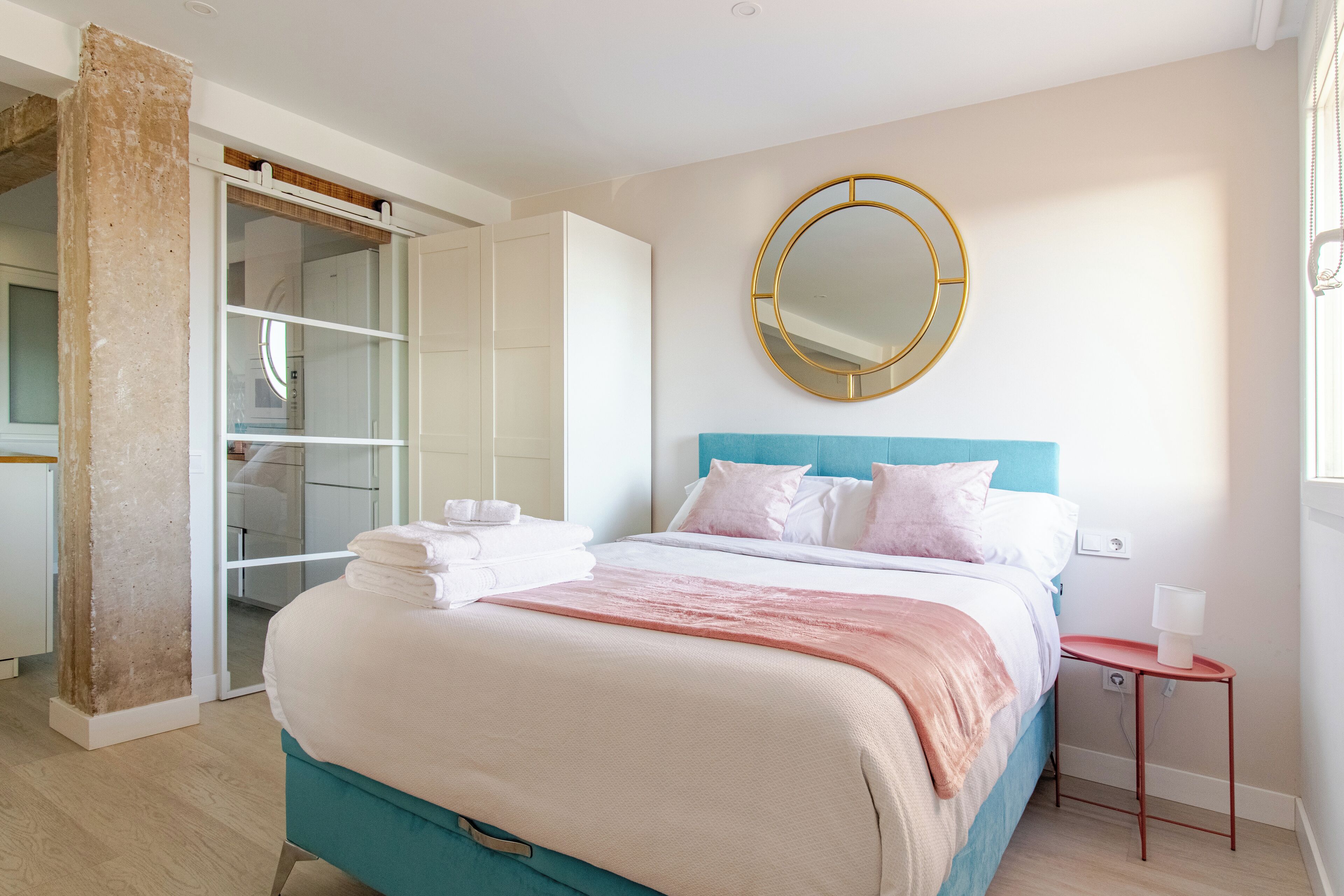 Een slaapkamer met een bed, een ronde spiegel, een nachtkastje en een kledingkast.
