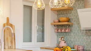 Een moderne keuken met een houten aanrecht, witte barkrukken, hangende pendelverlichting en een schaal fruit.