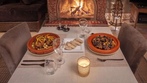 A dining table set with plates of food, glasses, and a candle, in front of a fireplace. - RIAD BOHEMIA (Marrakech)