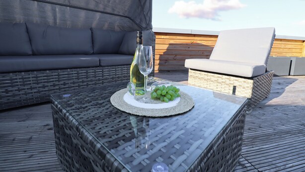 A rooftop seating area with a glass table, a bottle of wine, and a plate of grapes.