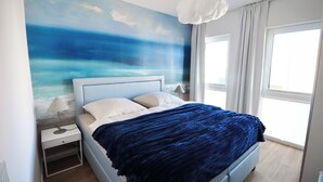 A bedroom with a bed, a nightstand, a lamp, and a large window.