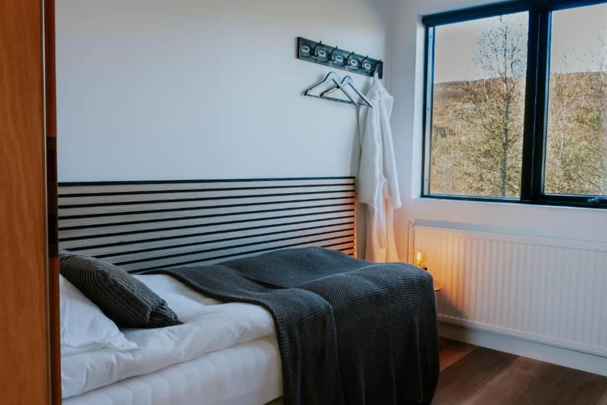 A bedroom with a bed, a radiator, a window with a view of trees, and a coat rack with hangers.
