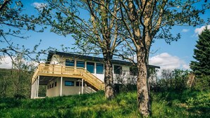 Ett modernt hus med en träbalkong, omgivet av frodig grönska och träd.
