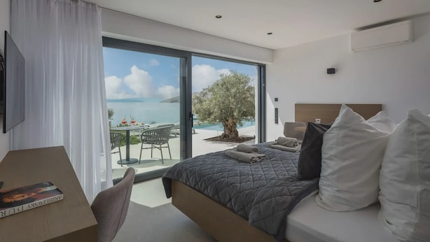 A modern bedroom with a large bed, a desk, and a view of the sea.