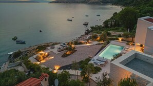 A coastal property with a swimming pool, outdoor seating, and boats on the water.