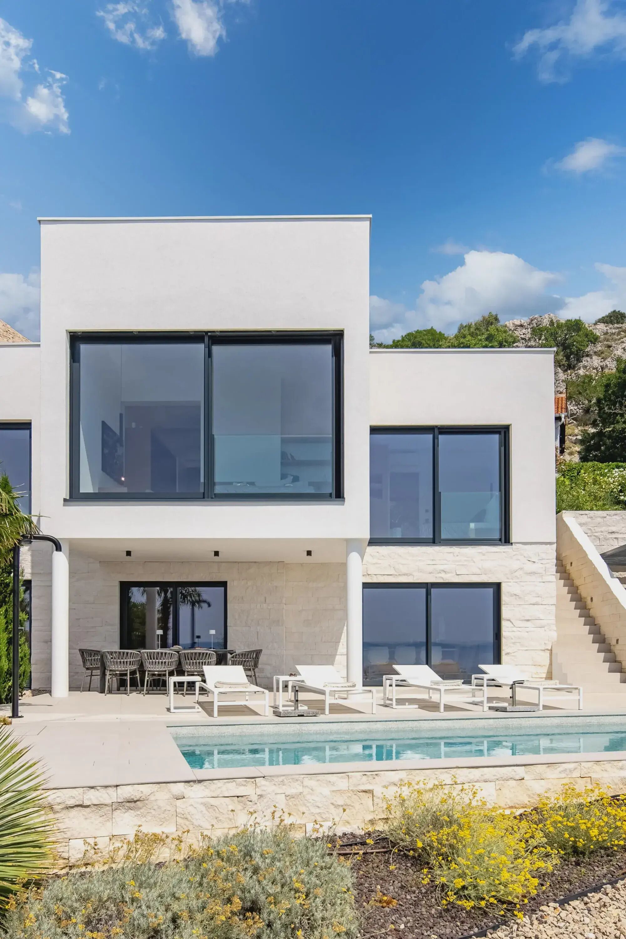 A modern two-story house with a swimming pool, outdoor seating, and a stone facade.