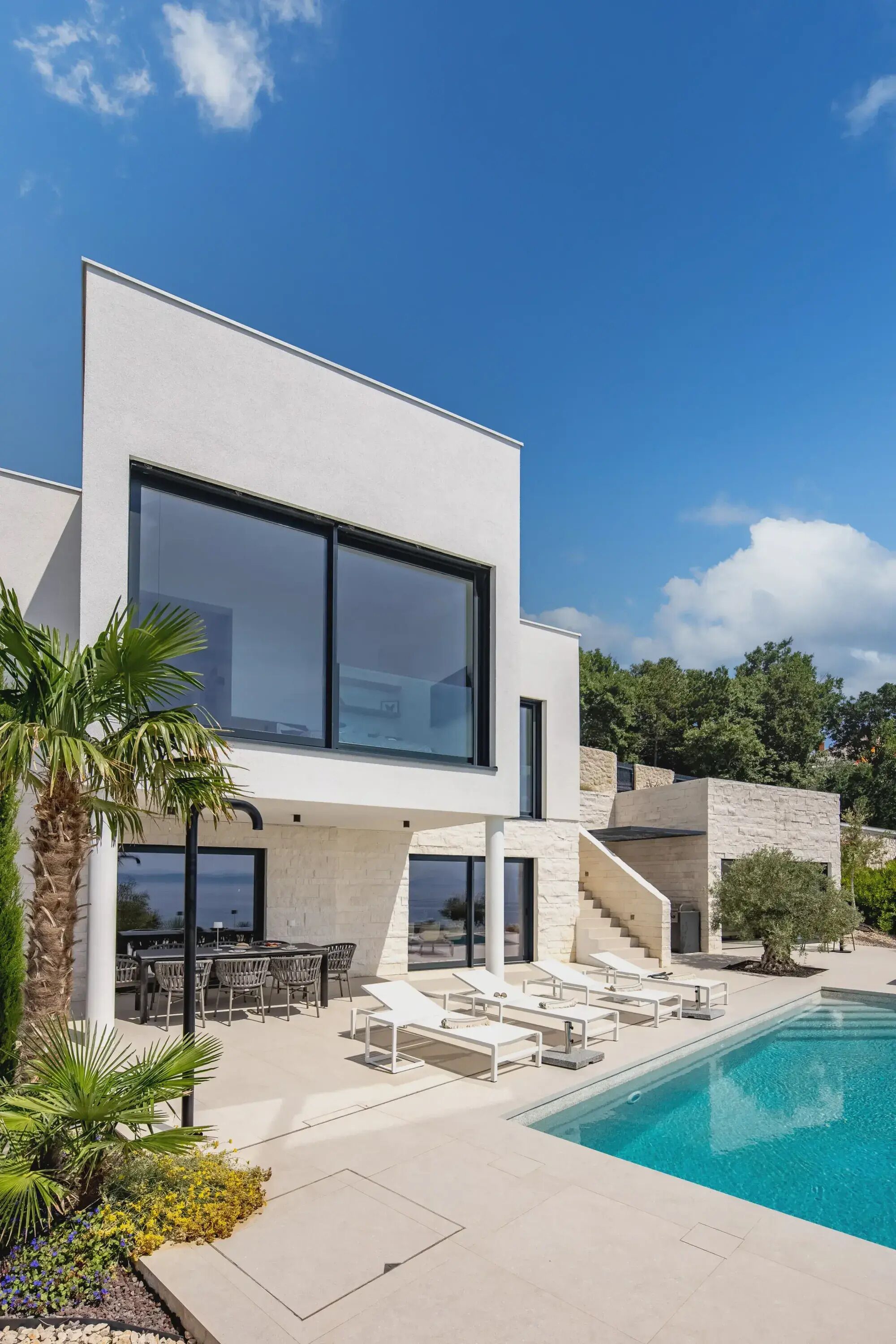 A modern house with a swimming pool, outdoor seating, and a staircase leading to a second floor.