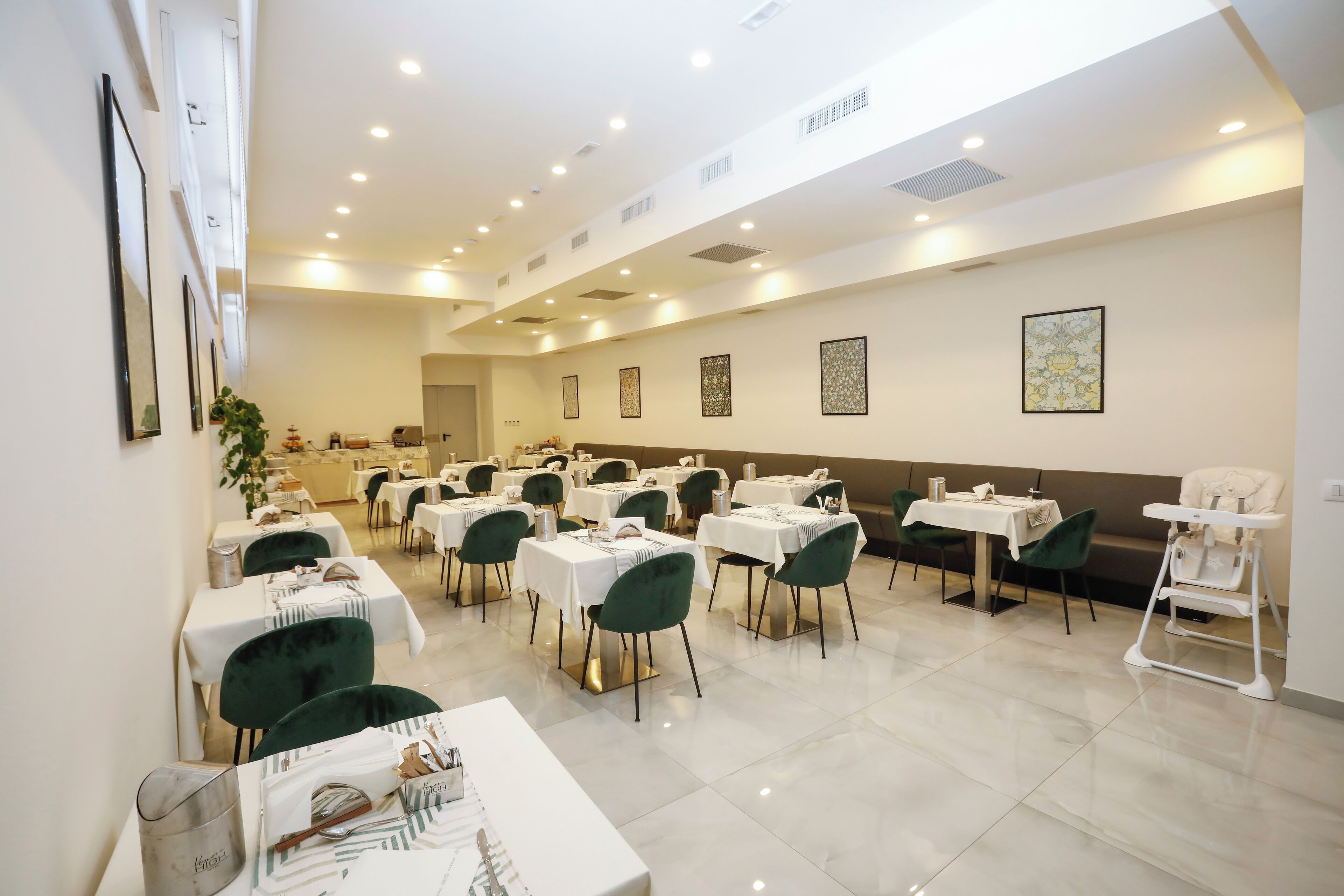 A spacious dining area with multiple tables and chairs, a high ceiling with recessed lighting, and framed artwork on the walls.