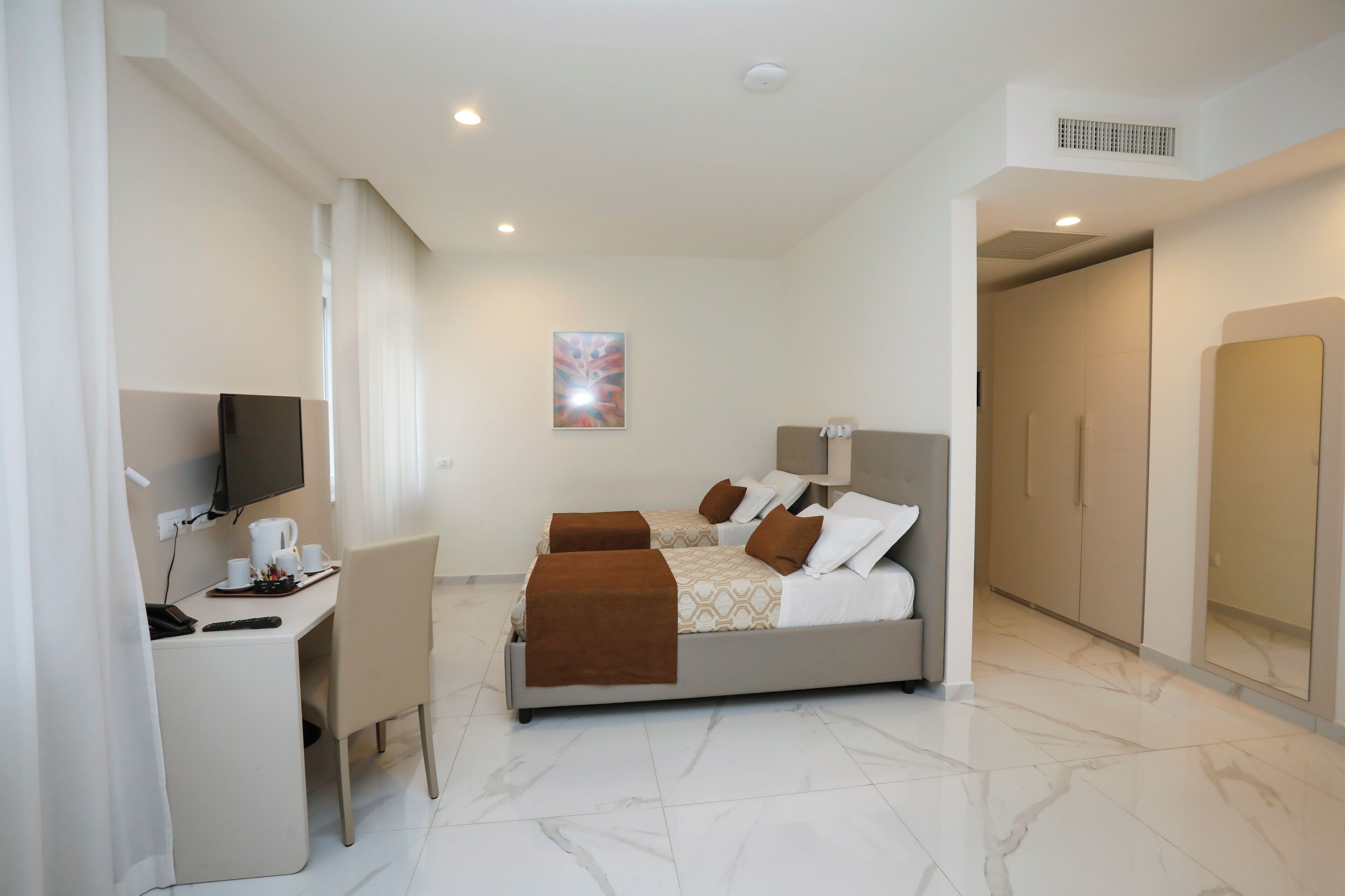 A modern hotel room with a bed, a desk with a chair, a television, and a painting on the wall.