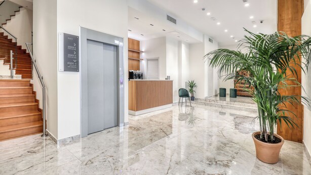 A modern lobby with a marble floor, a reception desk, a staircase, and a potted plant. - Vomero High Hotel (Naples)