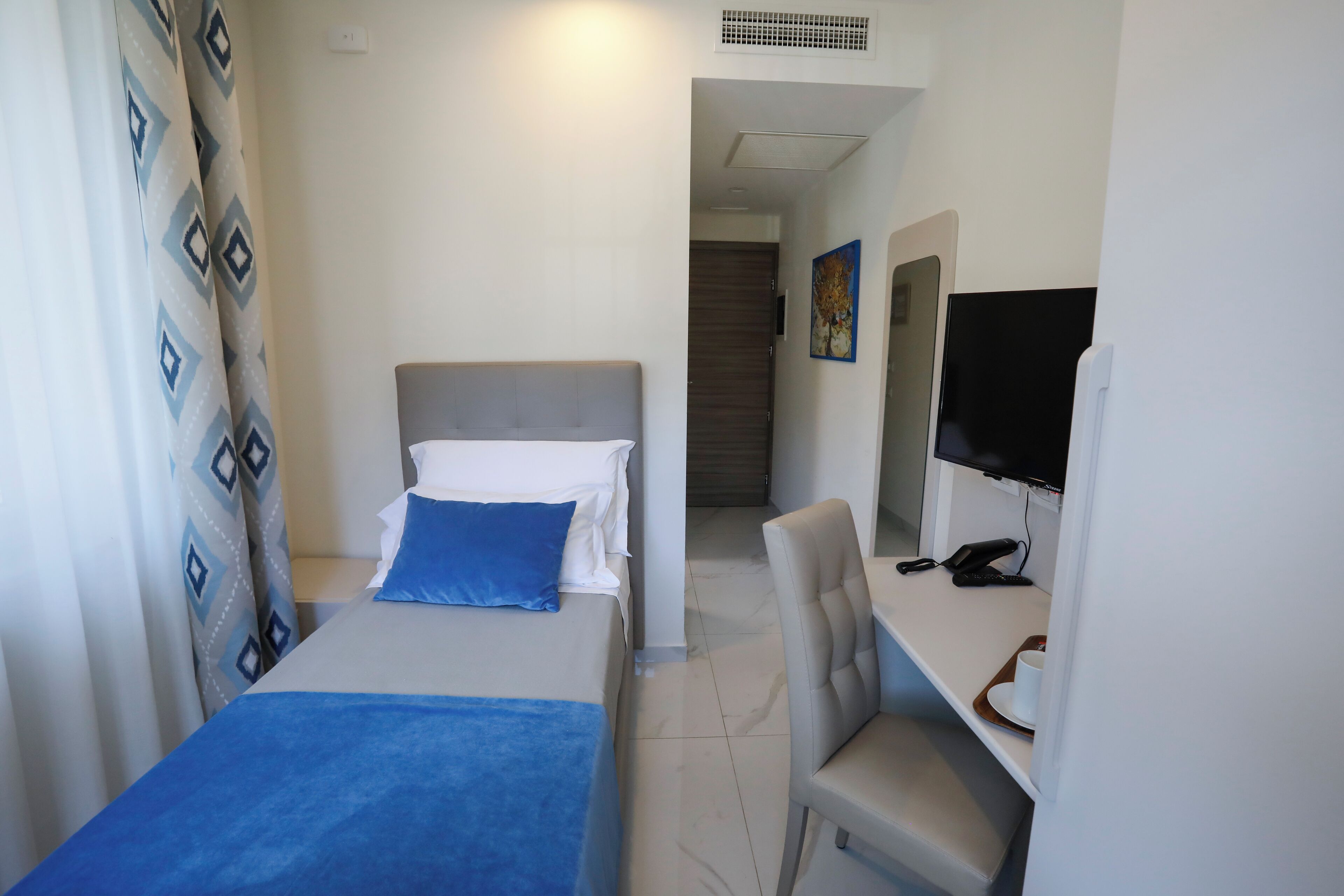 Une chambre d’hôtel avec un lit, un bureau équipé d’un ordinateur et un téléviseur.