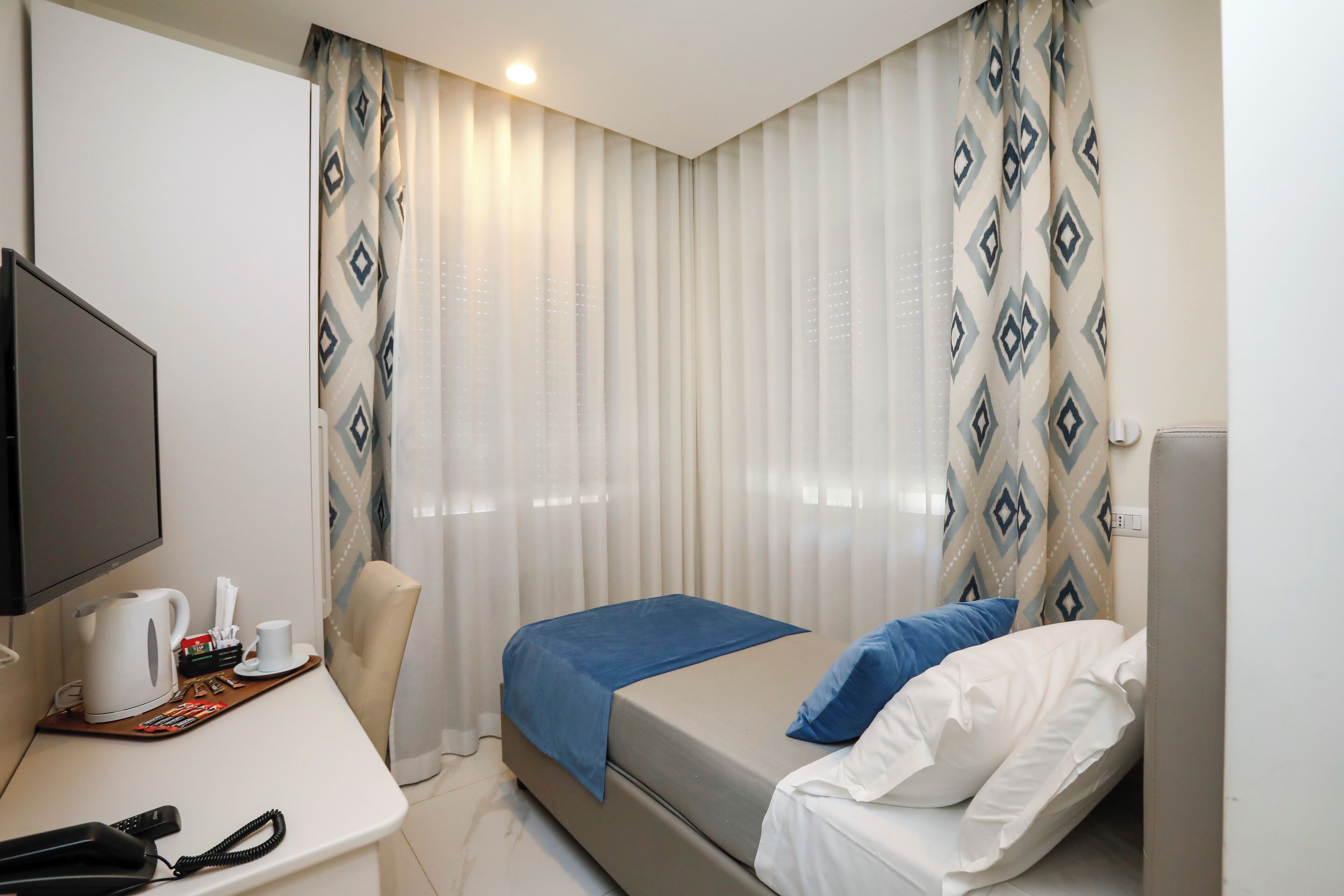 A hotel room with a bed, a desk with a telephone, a coffee maker, and a TV.