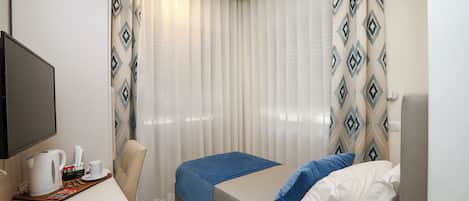 A hotel room with a bed, a desk with a telephone, a coffee maker, and a TV.