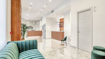 A modern lobby with a green sofa, a reception desk, and a potted plant.