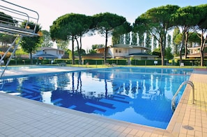 Une piscine à l’eau d’un bleu limpide, entourée d’arbres et de bâtiments.