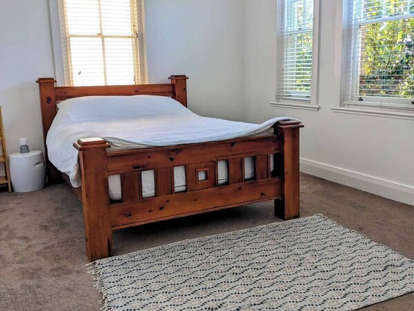 A wooden bed with a white mattress in a room with white walls and a window with blinds.