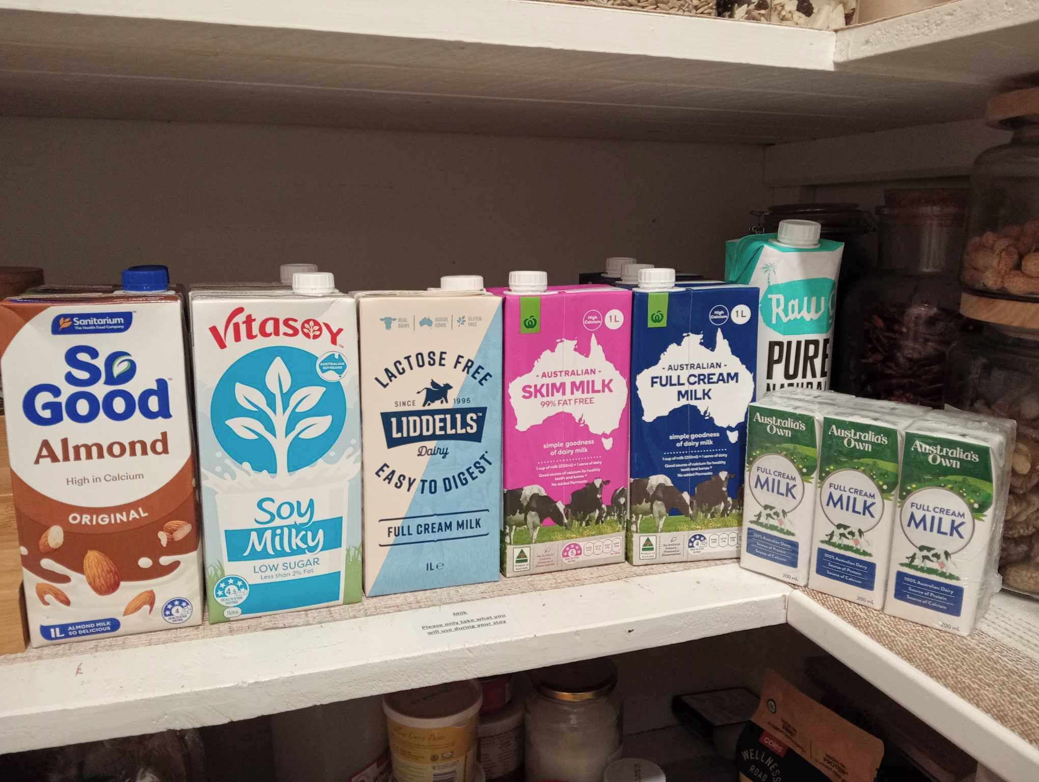 Een plank vol met verschillende pakken melk, waaronder merken zoals So Good Almond, Vitasoy, Liddell's lactosevrij en Australia's Own volmelk.
