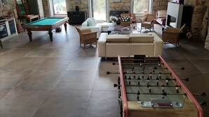 Uma sala de estar ampla com mesa de bilhar, mesa de futebol e um conjunto de sofás.