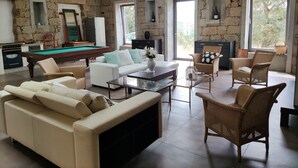 Uma sala de estar espaçosa com mesa de bilhar, assentos confortáveis e janelas amplas que proporcionam luz natural.