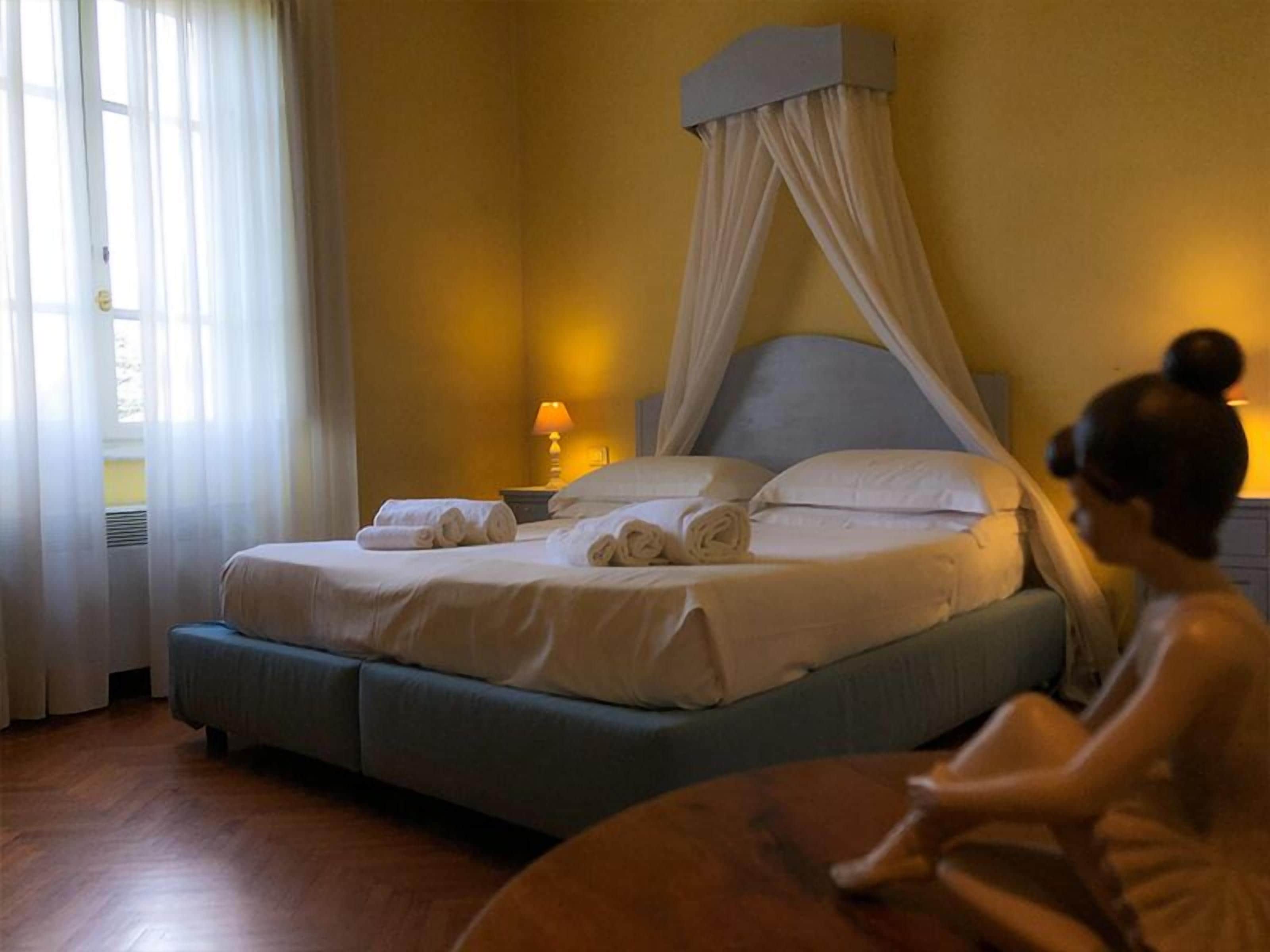 A hotel room with a bed, a nightstand, a lamp, and a window with curtains.