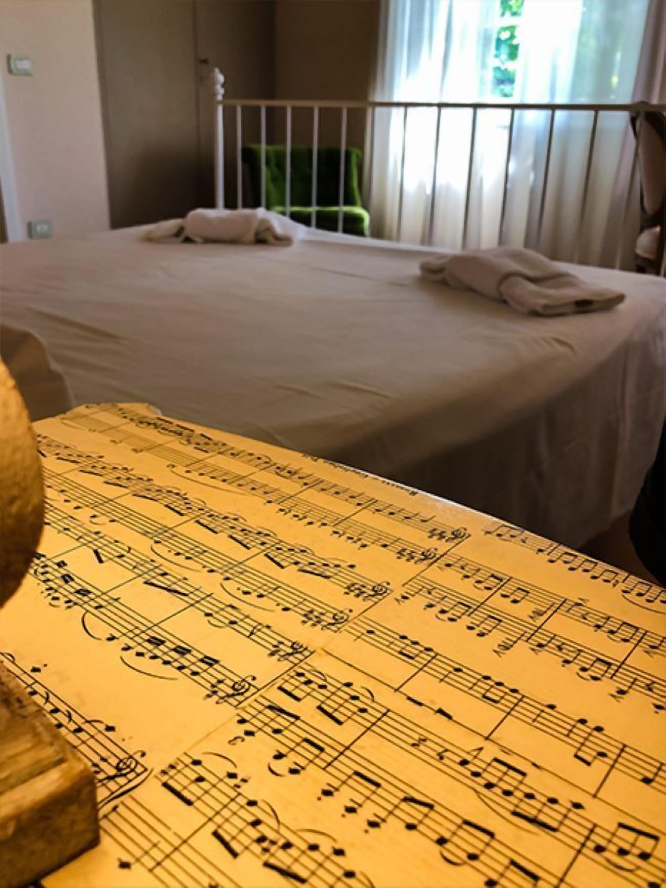 A hotel room with a bed, a window with curtains, and a table with a musical notes tablecloth.