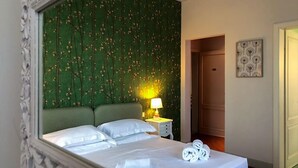 A hotel room with a large bed, green floral wallpaper, a bedside lamp, and a door leading to another room. - Villa Agnese Bed and Breakfast (Lucca)