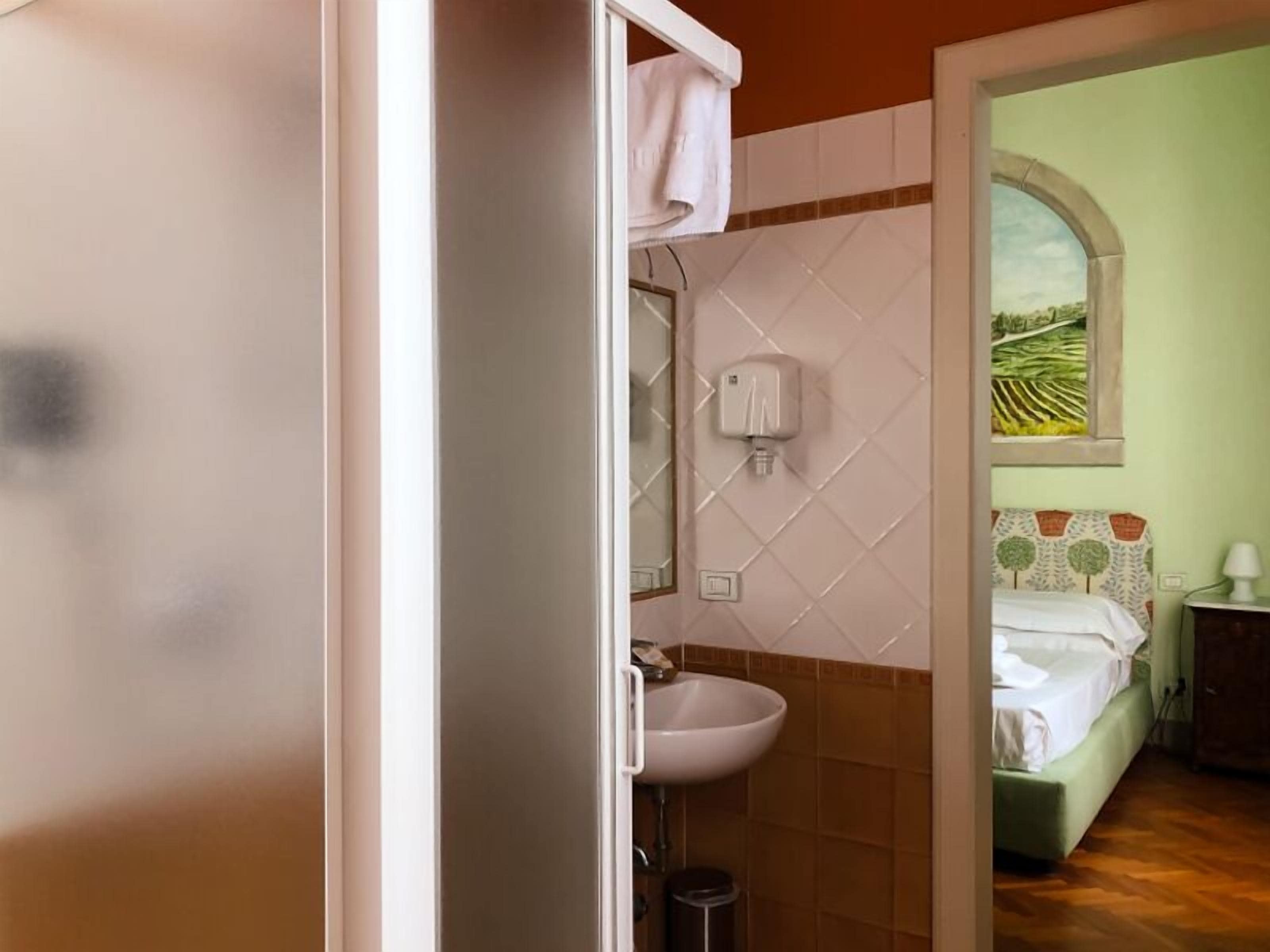 Un baño con un lavamanos blanco, un espejo y un secador de manos. Se ve una ventana con vistas a un campo.