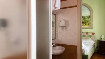 Un baño con un lavamanos blanco, un espejo y un secador de manos. Se ve una ventana con vistas a un campo.
