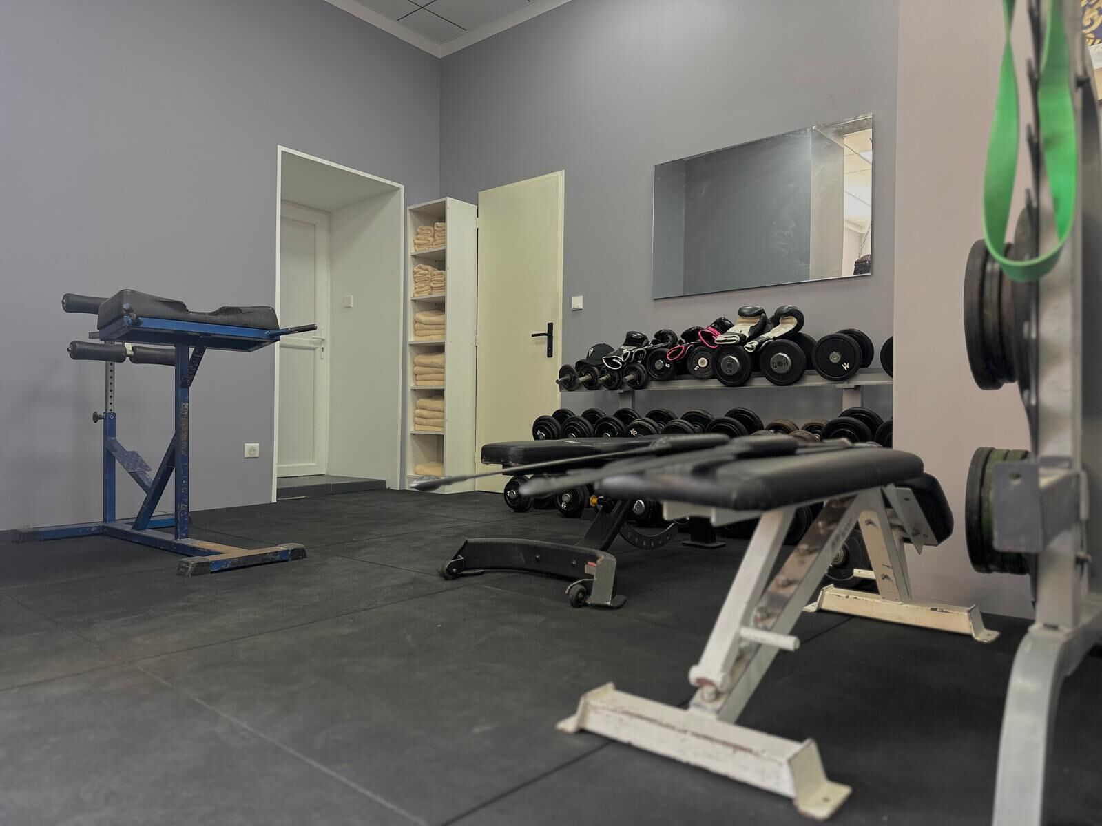 Un gimnasio con equipo de levantamiento de pesas, una banca y un estante con mancuernas.