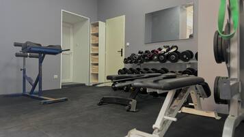 Un gimnasio con equipo de levantamiento de pesas, una banca y un estante con mancuernas.