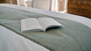 Una cama bien hecha con un libro abierto, un tocador con espejo y una puerta que da a otra habitación.