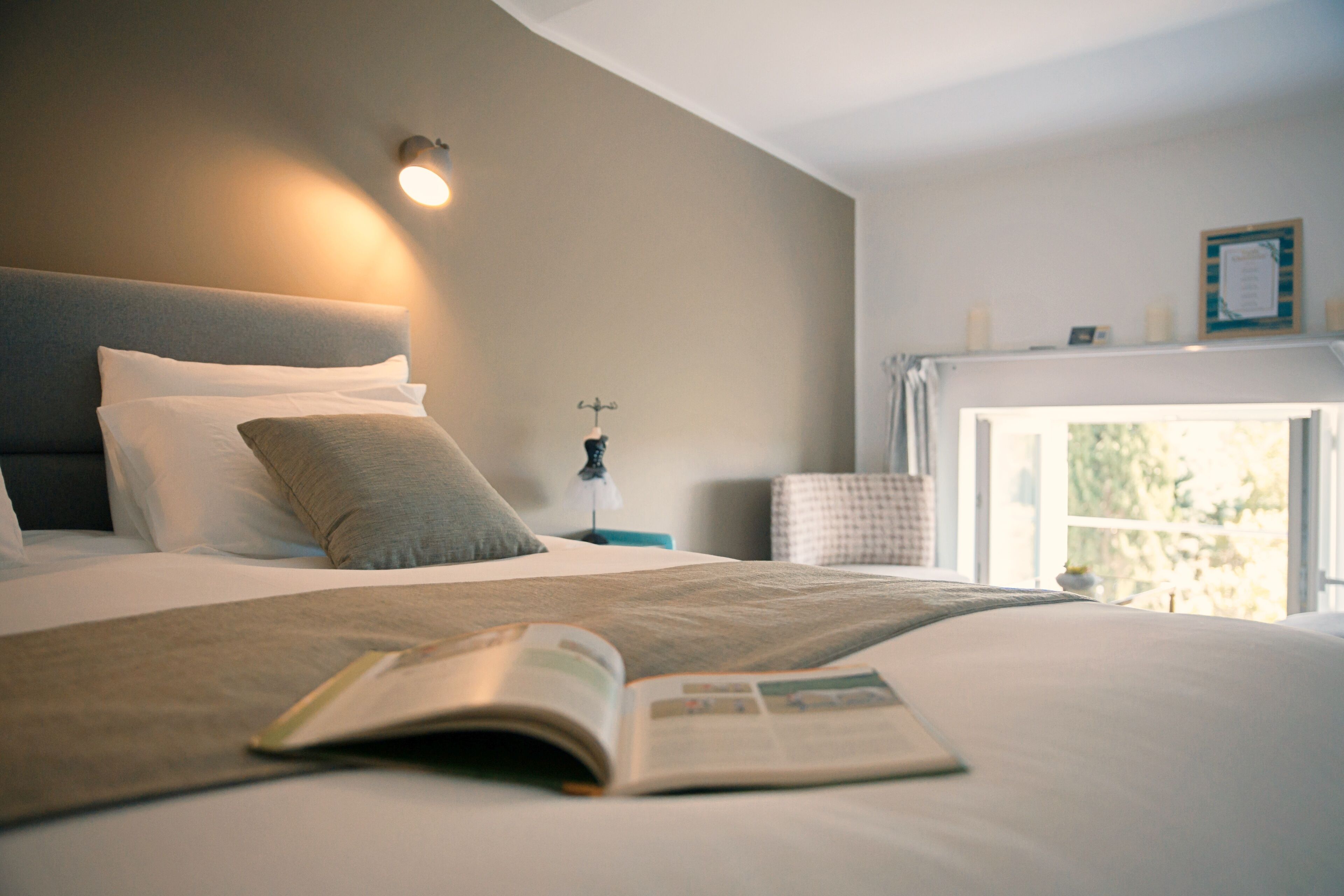 A neatly made bed with pillows, a bedside lamp, and a book on the bed.