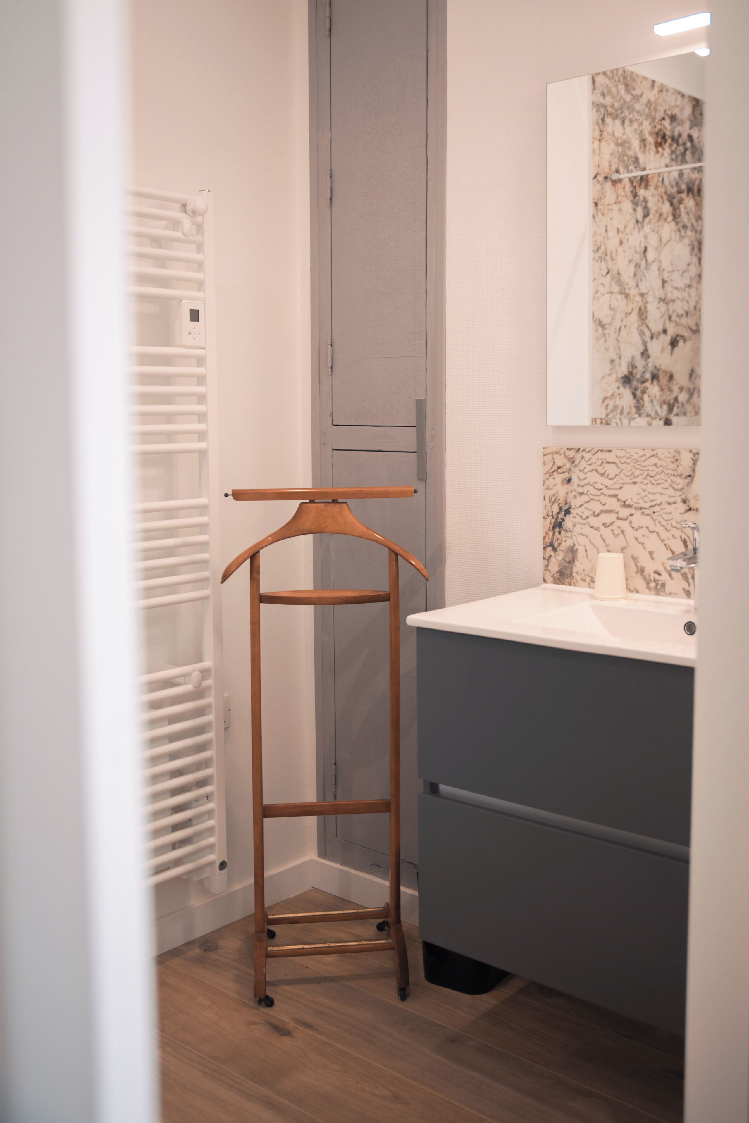 A bathroom with a wooden drying rack, a grey cabinet, and a marble backsplash.