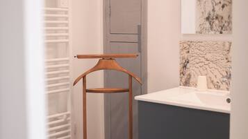 A bathroom with a wooden drying rack, a grey cabinet, and a marble backsplash.