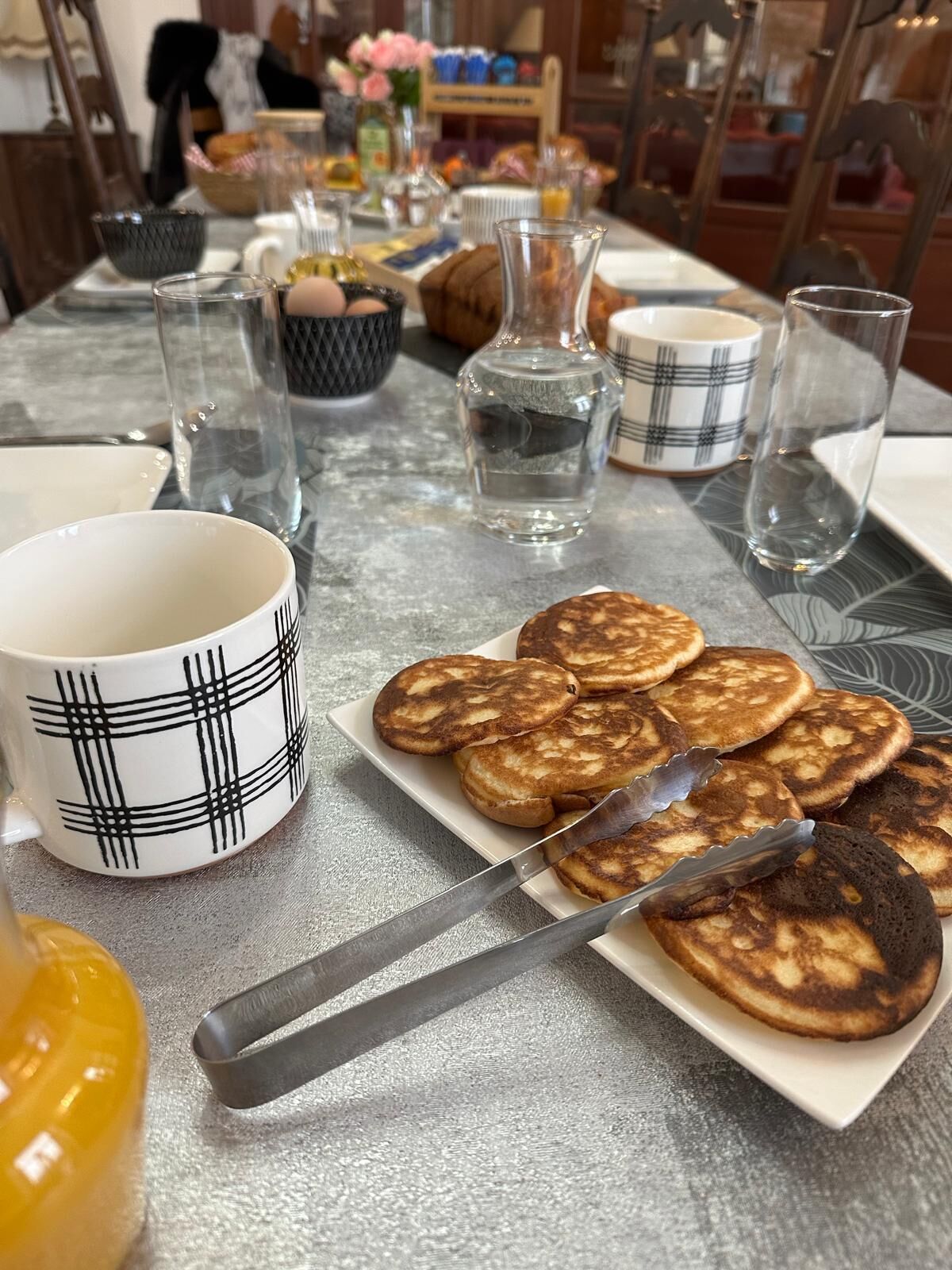 Een ontbijttafel met pannenkoeken, een karaf, een mok en een fles.