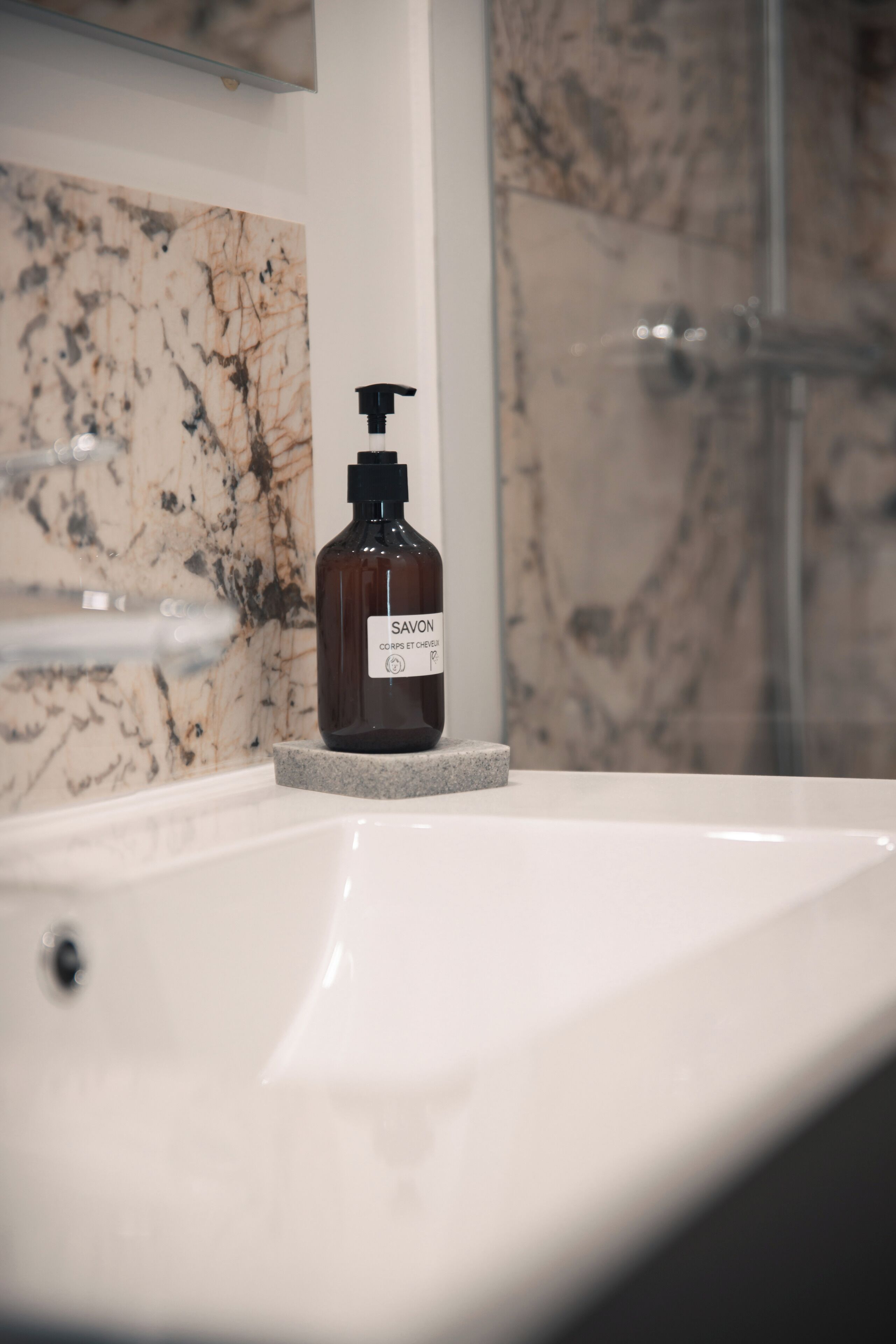 A bathroom with a marble wall, a white sink, and a bottle of Savon soap on the sink.