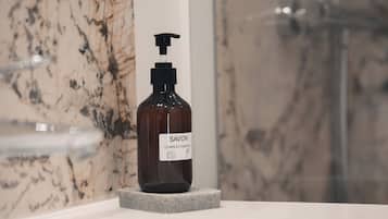 A bathroom with a marble wall, a white sink, and a bottle of Savon soap on the sink.