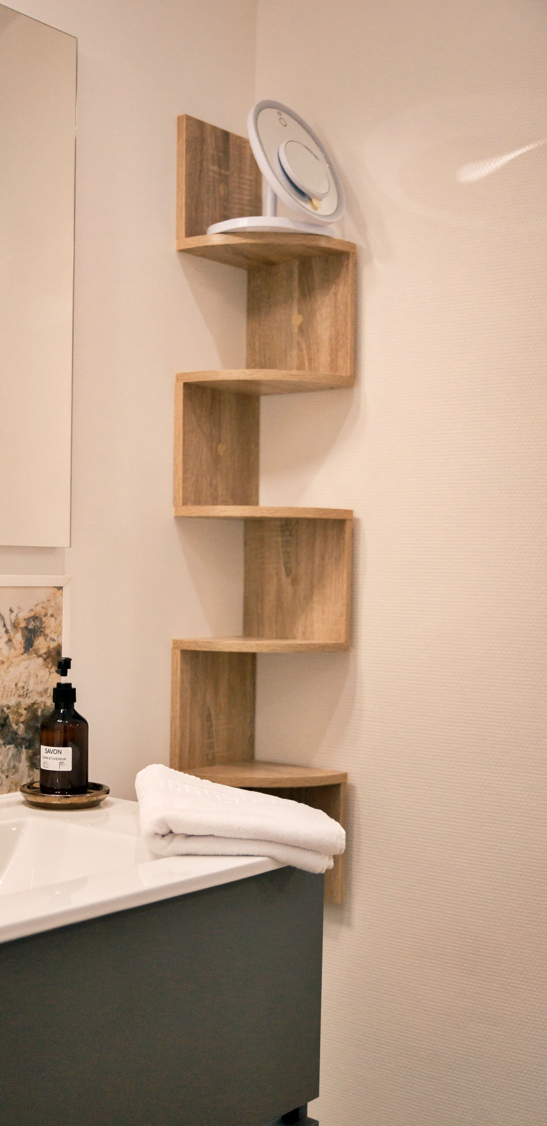A bathroom with a wooden shelf unit, a mirror, a bottle of soap, and a towel on a sink.