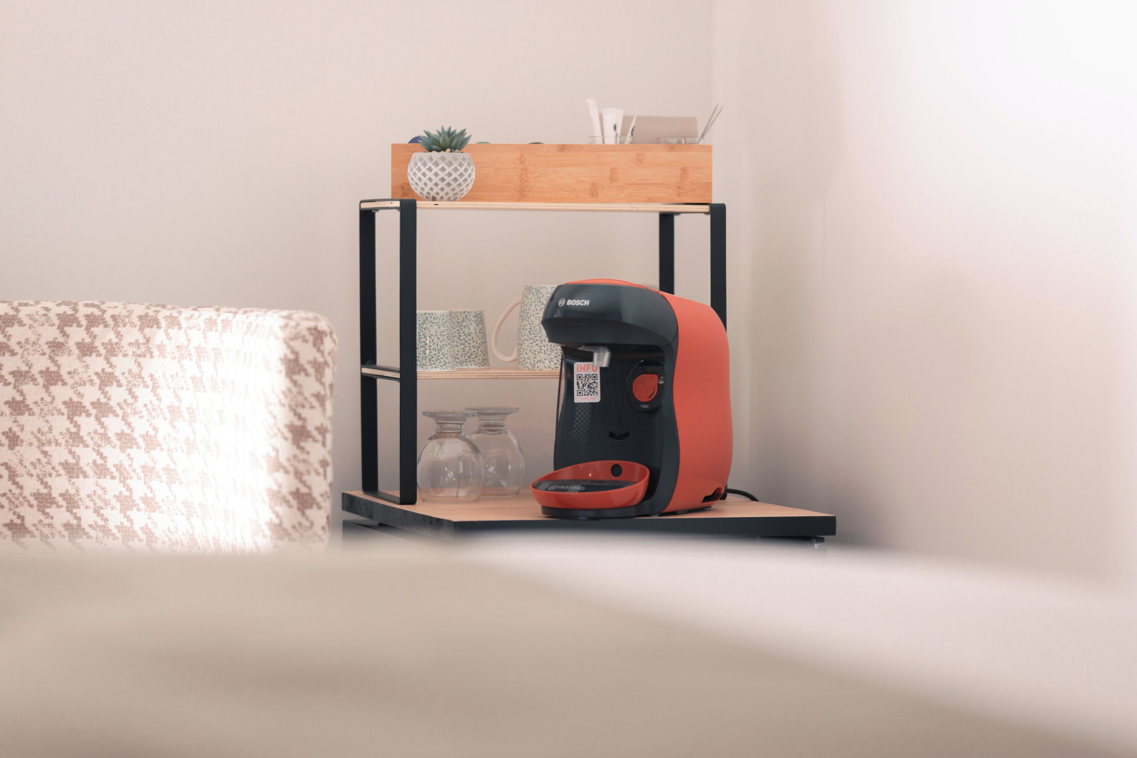 Una cocina moderna con una cafetera Bosch sobre una repisa de madera, un sofá estampado y una pequeña planta en maceta.