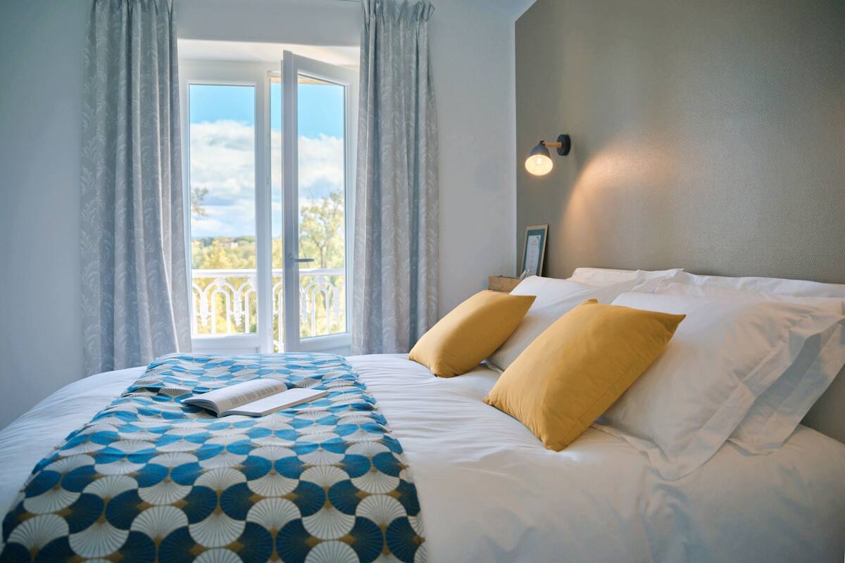A neatly made bed with a patterned bedspread, two pillows, and a book on it.