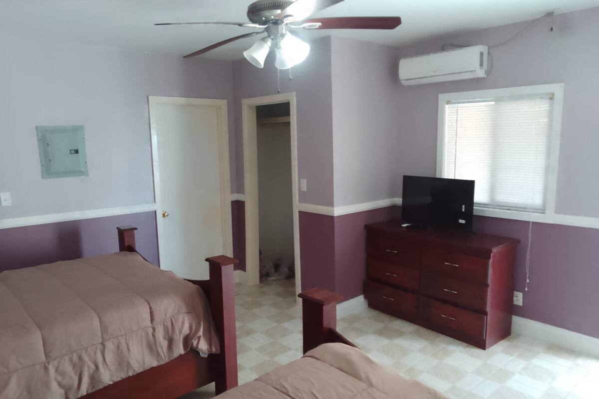 A bedroom with two beds, a ceiling fan, a TV on a dresser, and an air conditioning unit.