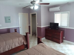 A bedroom with two beds, a ceiling fan, a TV on a dresser, and an air conditioning unit. - Alvira's Place (Little Creek)