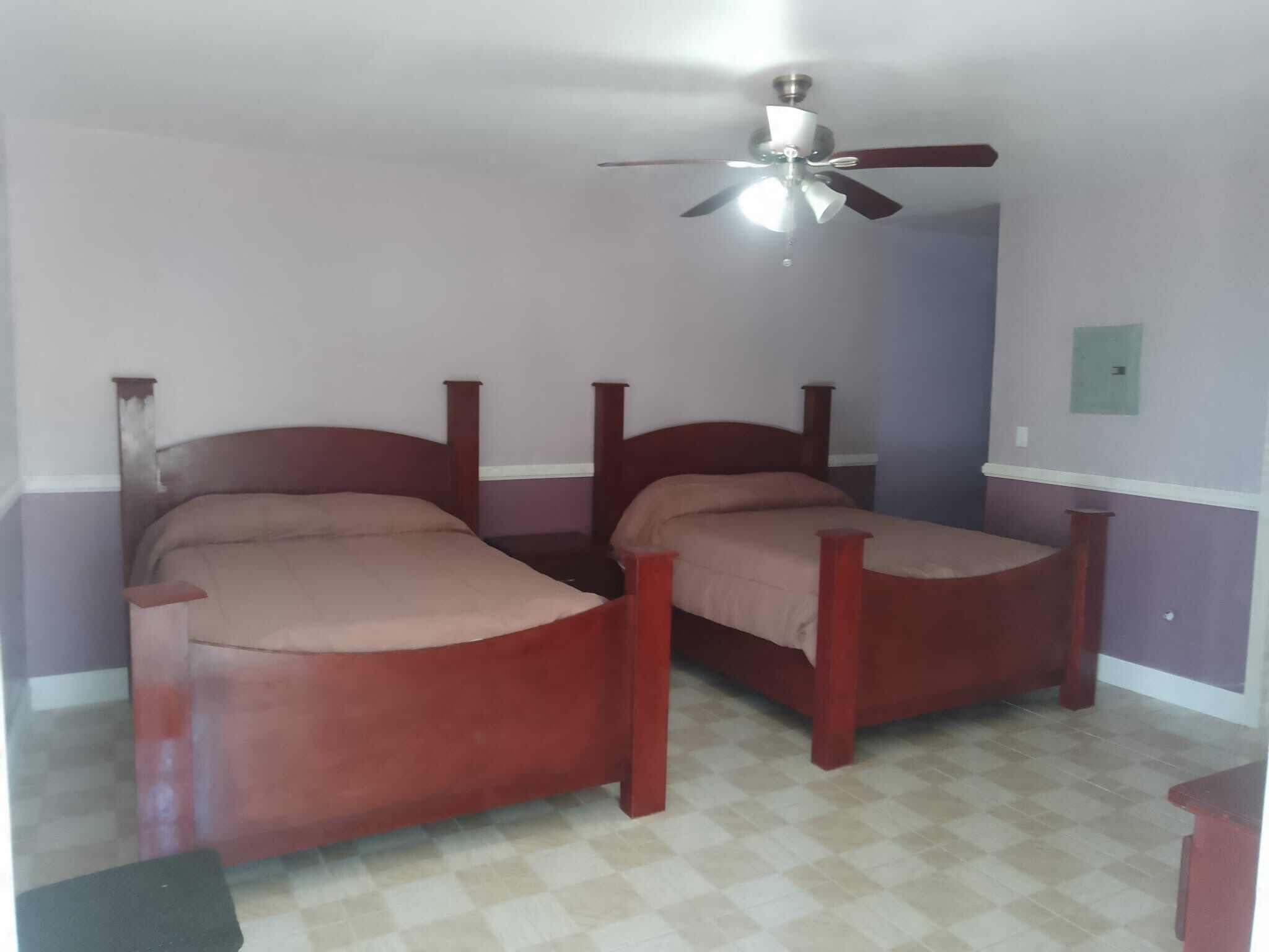 A room with two wooden beds, a ceiling fan, and a checkered floor.