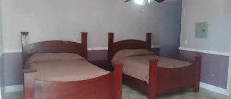 A room with two wooden beds, a ceiling fan, and a checkered floor.