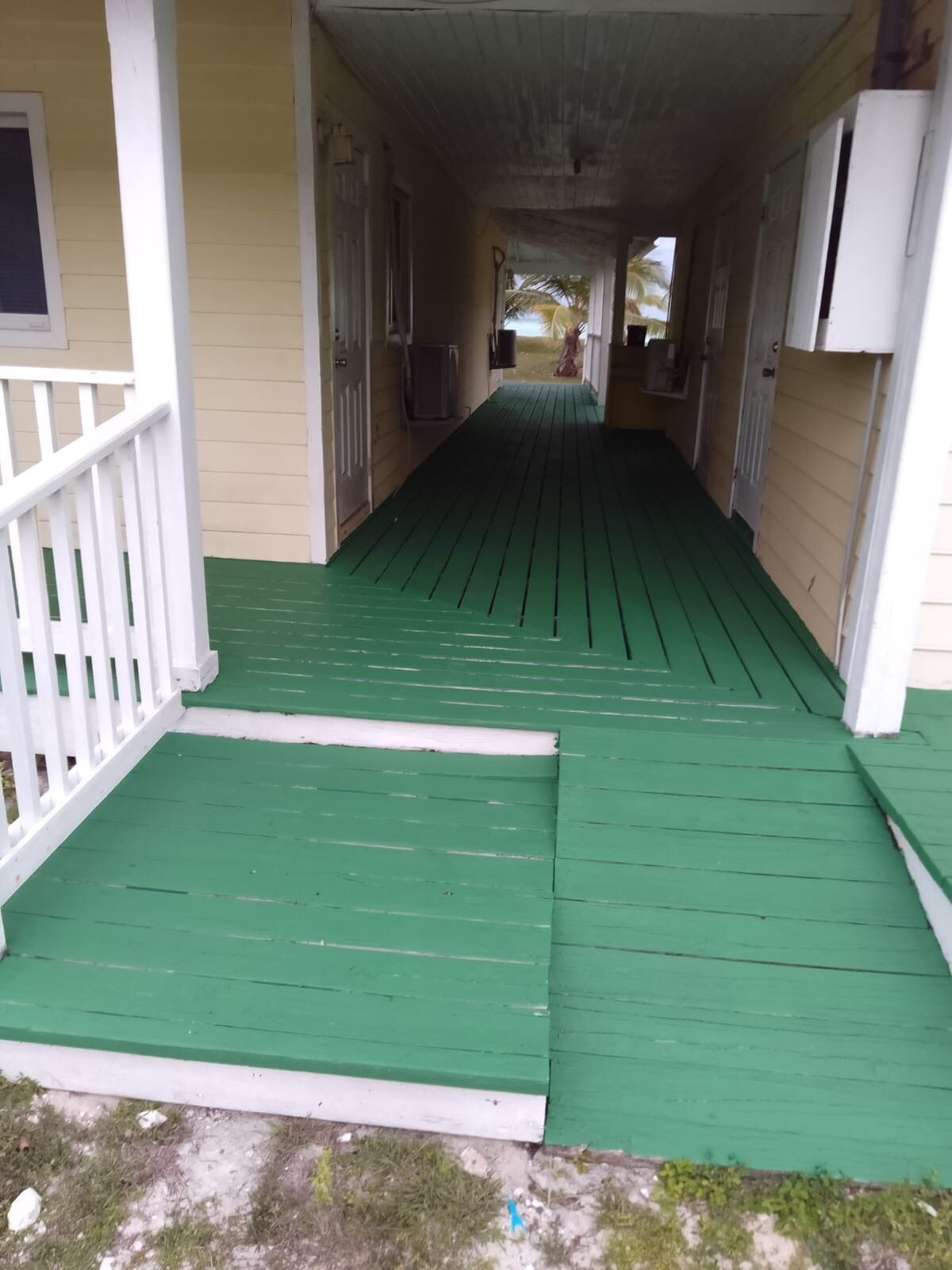 A covered porch with a green floor and white railings.