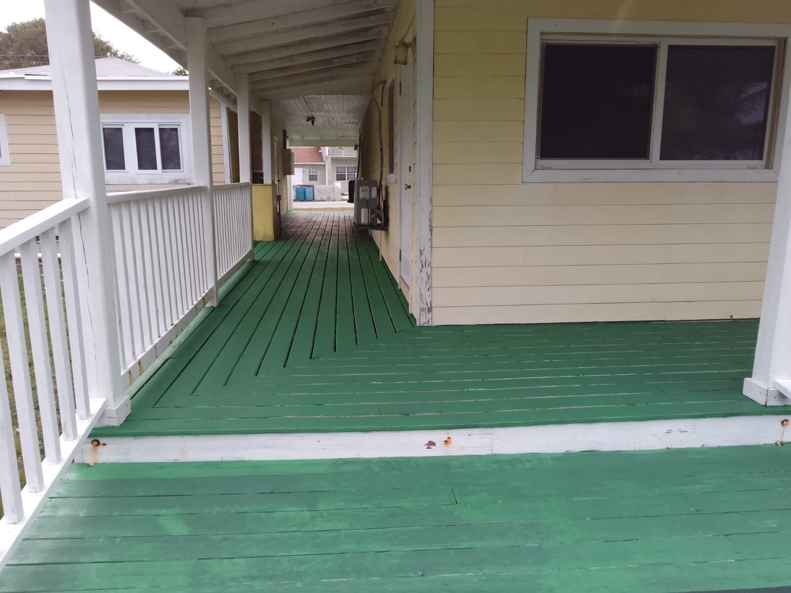 Een overdekte veranda met een groene vloer en witte leuningen.