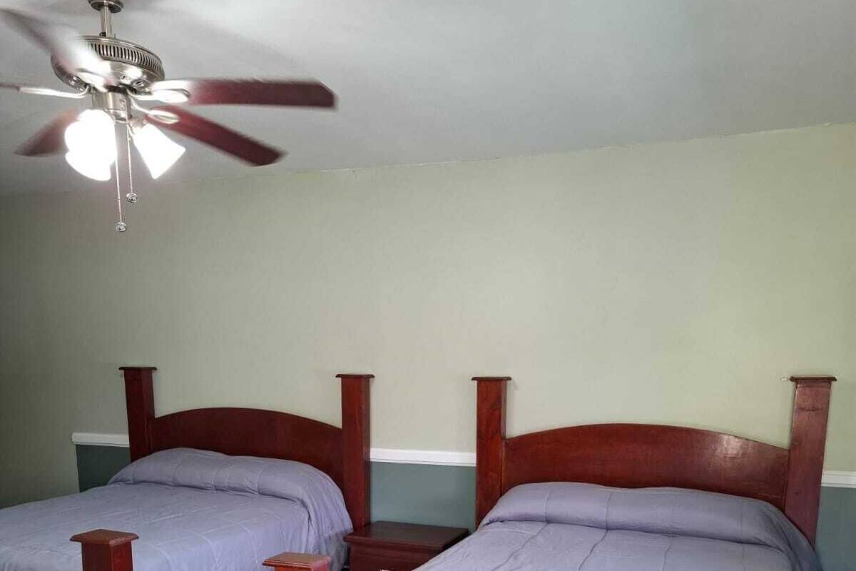 A bedroom with two wooden beds, a ceiling fan, and a checkered floor.